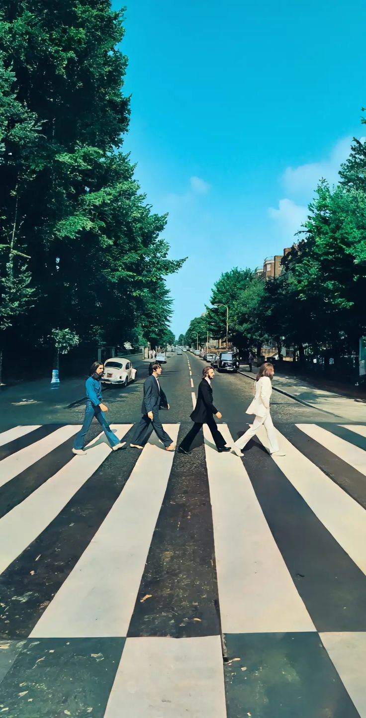 the beatles walking across a crosswalk in front of some trees and buildings on a sunny day