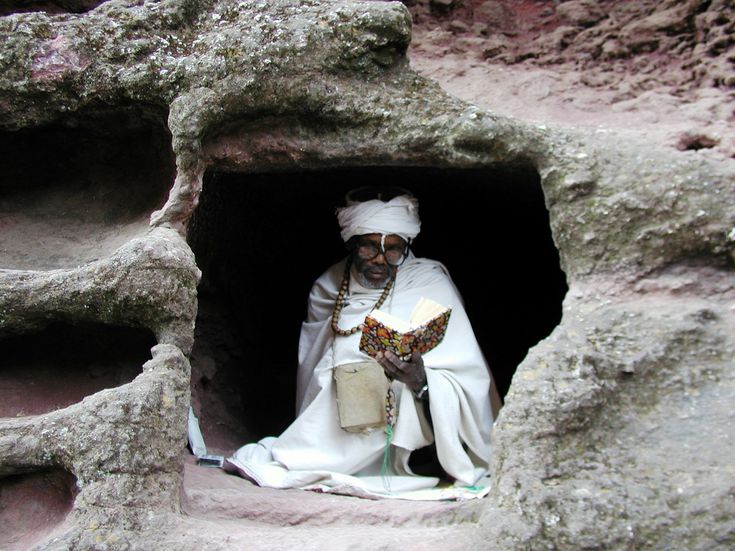 a man dressed in white holding a book and wearing a crown is sitting in a cave