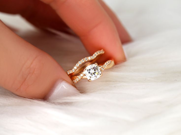 a woman's hand holding a diamond ring on top of white furnishing