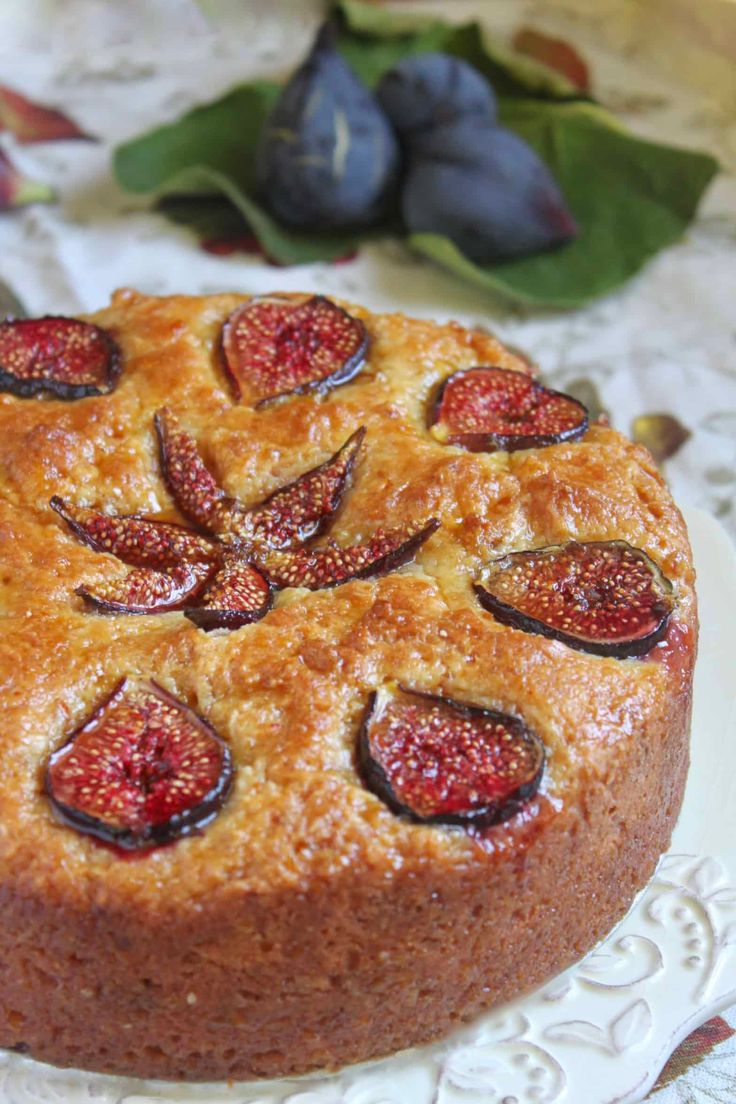 a close up of a cake on a plate with figs and flowers in the background