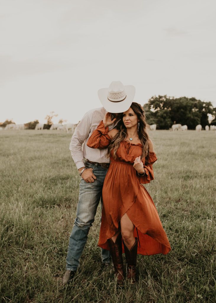 a man and woman are standing in the middle of a field wearing cowboy hats, orange dresses