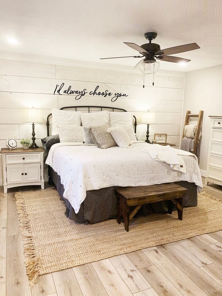 a bedroom with white walls and wood flooring has a bed, nightstands, and ceiling fan