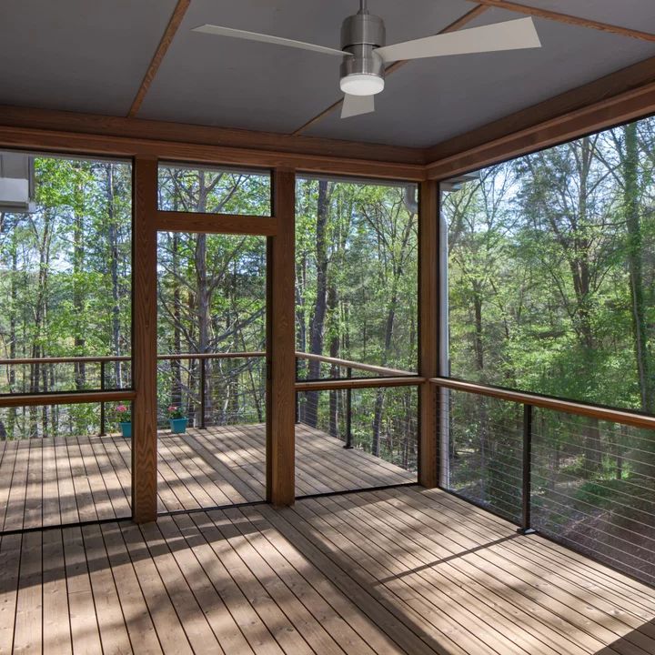 an empty screened porch with wood flooring and ceiling fan in the middle of it