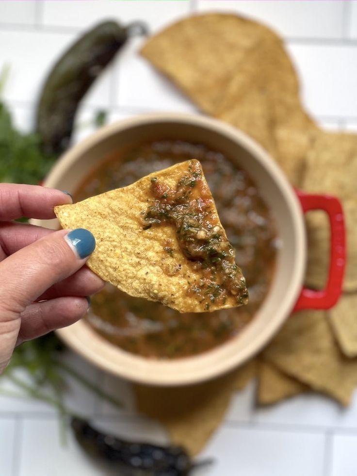 a hand holding a tortilla chip over a bowl of chili and beans soup