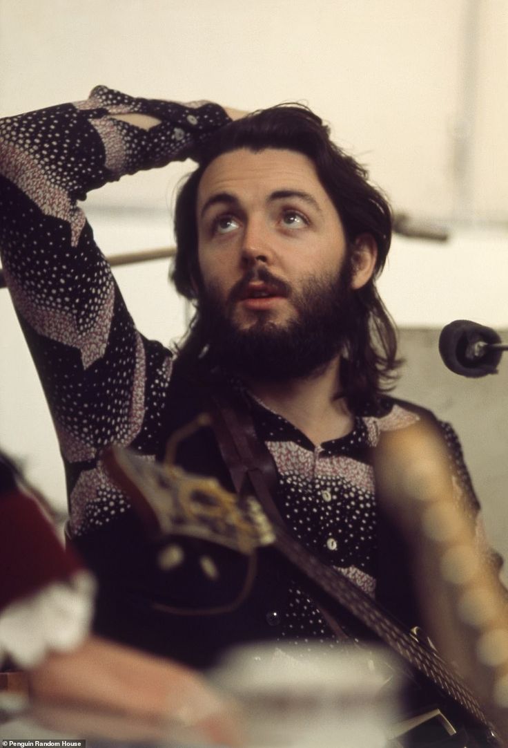 a man with long hair and beard holding a guitar in his hand while sitting at a table