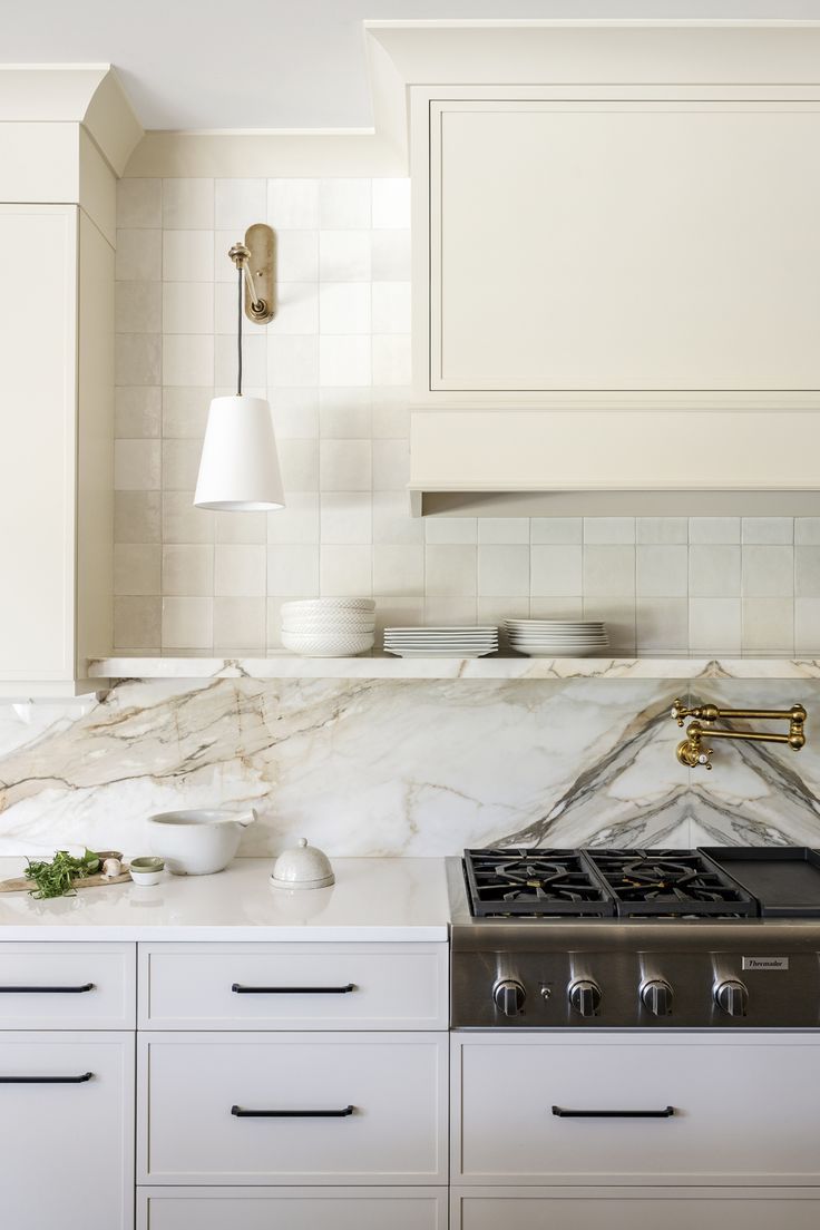 a kitchen with marble counter tops and white cabinets, gold faucet lighting over the stove