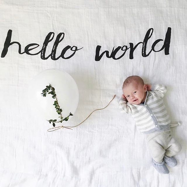 a baby laying on top of a bed next to a balloon with the word hello world written on it