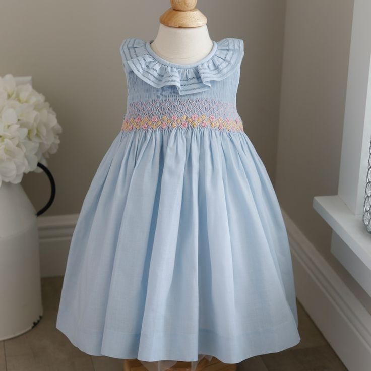 This Precious Luli & Me Dress Is Perfect For Spring!! The Pastel Blue Dress Is Sleeveless And Has A Ruffled Collar. The Collar Has Special Details In That It Has Three Rows, Each Hand-Faggoted Together (A High-End Stitch Found In Heirloom Clothing). The Bodice Is Smocked In An Accordion Smocking With Pink Embroidery Done In A Lattice Design. At The Waist Sits Two Rows Of Pink Embroidered Flowers Stretching From One Side To The Other. In Between The Layers Are Little Yellow Embroidered Daisies Wi Fitted Blue Smocked Dress For Playtime, Blue Embroidered Cotton Smocked Dress, Cute Sleeveless Dress With Smocked Cuffs, Blue Cotton Smocked Playtime Dress, Blue Dress With Smocked Bodice For Playtime, Spring Baptism Dress With Smocked Back, Blue Smocked Dress With Cuffs For Playtime, Blue Smocked Dress With Smocked Cuffs For Playtime, Cute Blue Smocked Dress With Ruffles