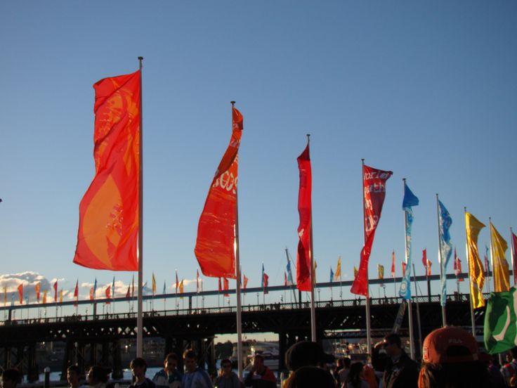 many flags are flying in the air near a bridge