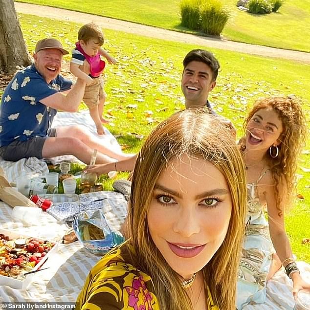 a group of people sitting on top of a grass covered field next to a tree