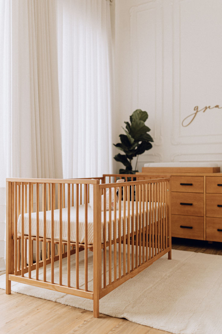 a wooden crib sitting in front of a window next to a dresser and bed