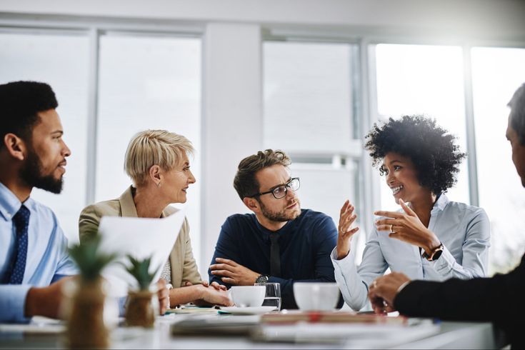 four people sitting at a table having a discussion with each other and one person holding his hand out