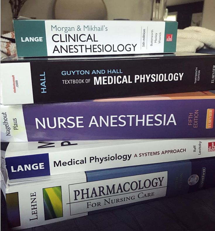 a stack of medical books sitting on top of a table next to a laptop computer