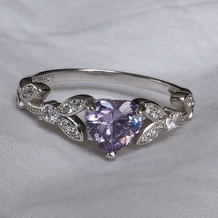 Brilliant sparkle with a captivating Lavender Cubic Zirconia heart shaped stone, this White Gold promise ring has a core of solid 925 Sterling Silver, making it hypoallergenic and built to last! The high-quality faceted lavender heart stone is 6mm (0.8 carat) and has a Mohs hardness of 8-1/2. Sprinkled generously with cubic zirconia rhinestones, this enchanting ring is accented by a nature-inspired tree branch and leaf design. It would make a great promise ring or engagement ring, as well as an Lavender Cubic Zirconia Rings For Gift, Lavender Crystal Promise Ring, Amethyst Heart Ring For Valentine's Day, Elegant Purple Heart Promise Ring, Purple Heart-shaped Promise Jewelry, Silver Heart-shaped Birthstone Ring With Gemstone, Silver Heart-shaped Birthstone Ring, Purple Heart Ring For Promise, Fine Jewelry, Silver Heart Cut Amethyst Ring Gift