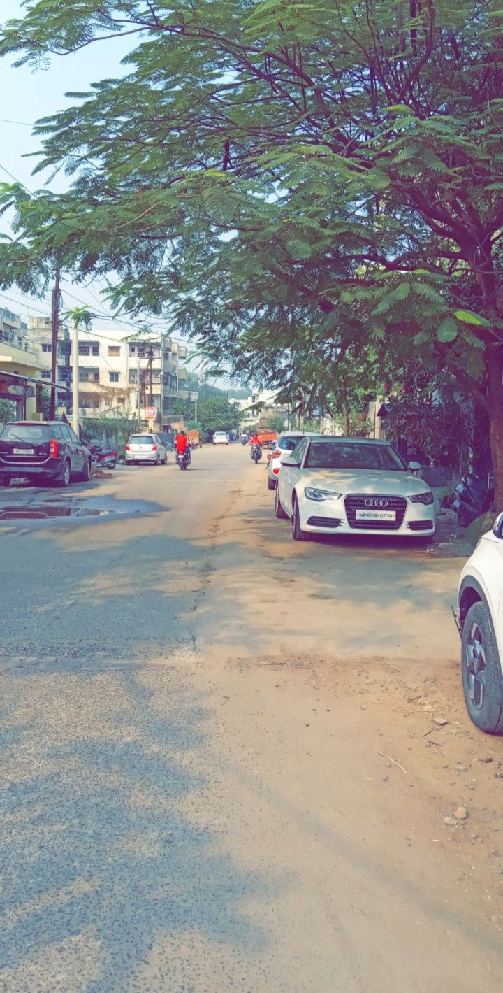 two cars parked on the side of a road next to trees and people walking down the street