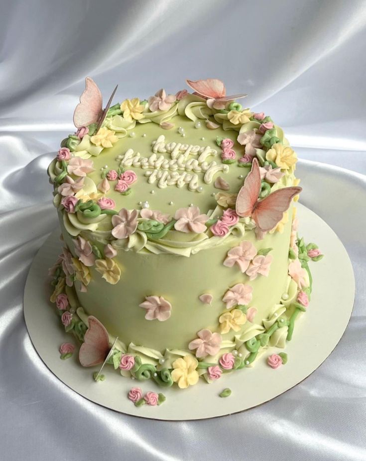 a birthday cake decorated with flowers and butterflies on a white tableclothed cloth background