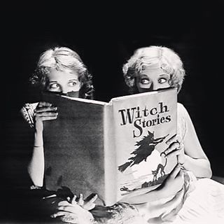 two women sitting on the floor reading a book together with their mouths open and eyes wide open