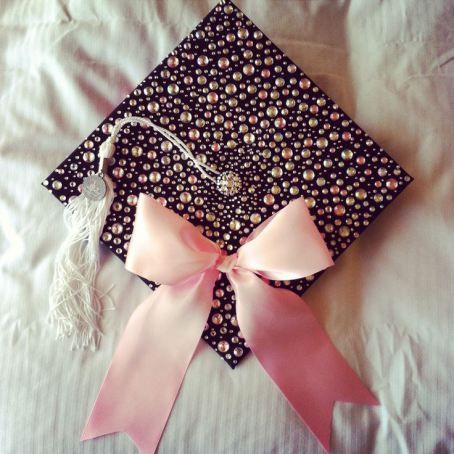 a graduation cap with a pink ribbon and tassel on top of it, sitting on a bed