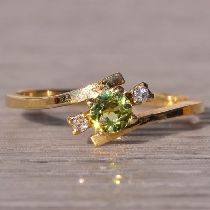 two gold rings with green and white stones on wooden table next to each other,