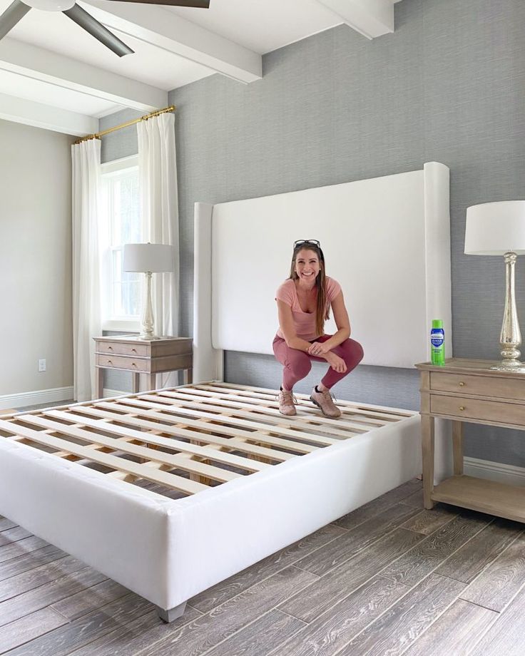 a woman kneeling on top of a bed in a room with wooden floors and white walls