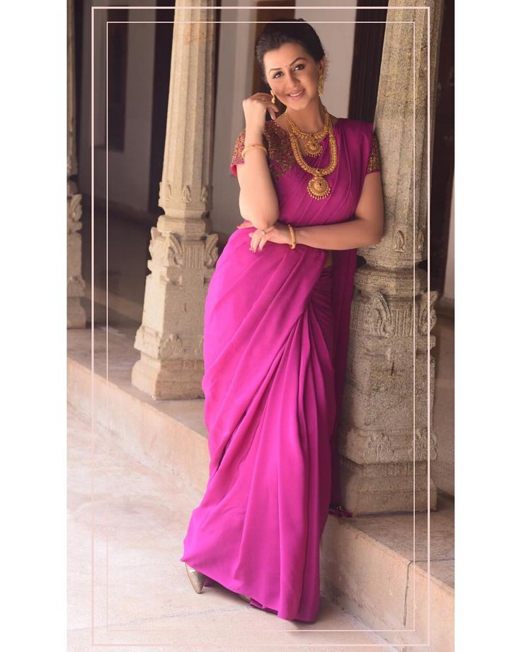 a woman in a pink sari leaning against a pillar with her hand on her hip