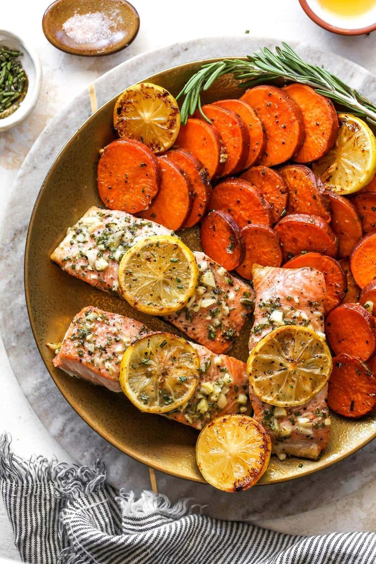 salmon and sweet potatoes on a plate with rosemary sprigs, lemons, and seasoning