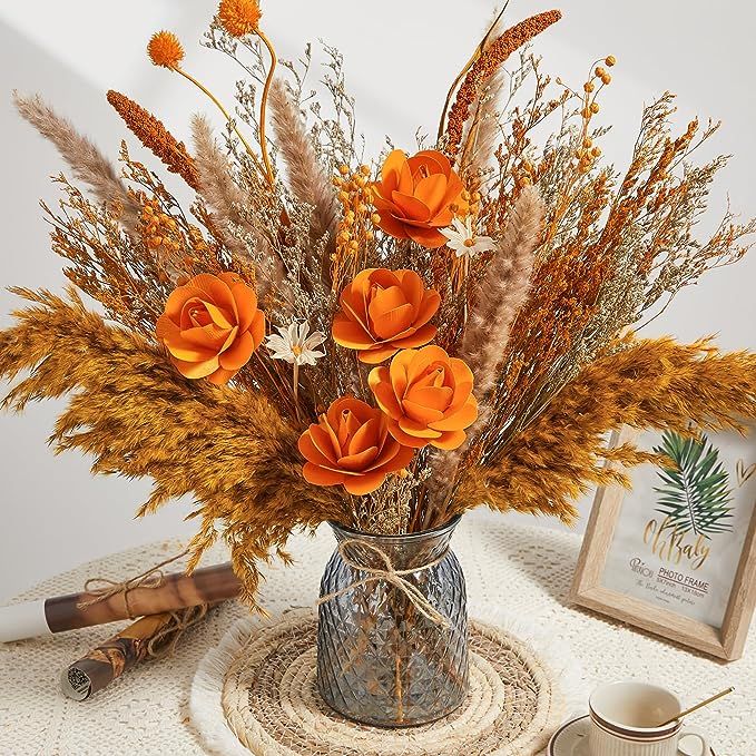 an arrangement of dried flowers in a vase on a table next to a coffee cup