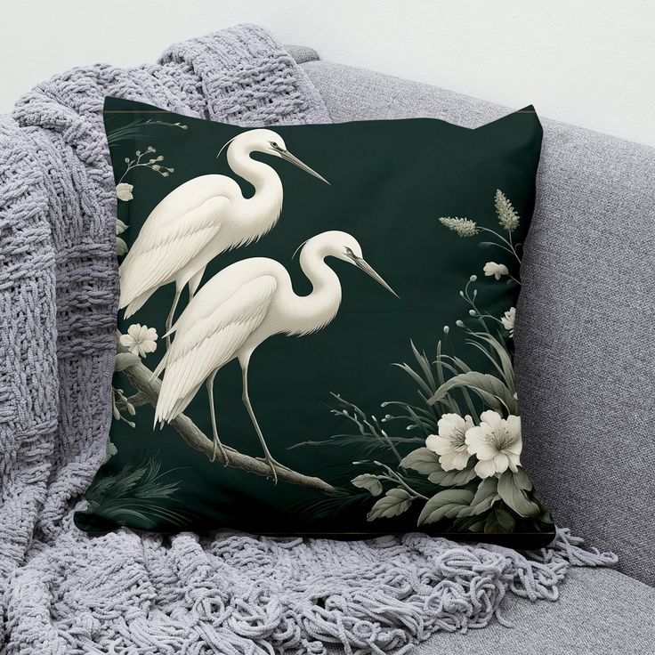 two white birds sitting on top of a green pillow next to a gray couch with flowers