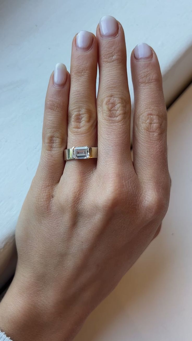 a woman's hand with a gold and white ring on her left hand, next to a window