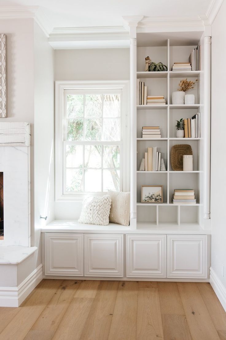 a living room filled with lots of white furniture and bookshelves next to a fire place