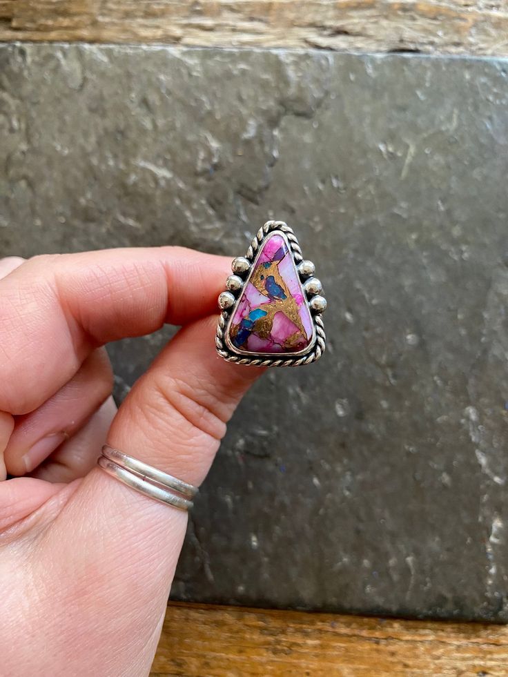 Handmade Spiny Oyster Shell + Purple Mohave Kingman Turquoise and sterling silver statement ring.  -Ring will fit US size 6.5 Vintage American Southwest style design. Striking pink, blue, purple and gold colored stone. Twisty rope trim, Hand polished, rustic looking patina and high polish finish. Hand stamped Indian style Arrow and Rising Sun hallmark on backside. Chunky, double split style ring shank/band.   Turquoise stone is a composite of different materials, and is sourced from Kingman Ariz Unique Turquoise Gemstone Ring, Unique Multicolor Jewelry With Large Stone, Unique Multicolor Large Stone Jewelry, Multicolor Cabochon Jewelry, Southwestern Style Pink Jewelry Gift, Unique Multicolor Sterling Silver Turquoise Ring, Multicolor Turquoise Ring In Sterling Silver, Unique Multicolor Turquoise Ring In Sterling Silver, Jewelry Purple