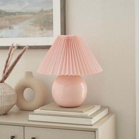 a pink lamp sitting on top of a table next to a vase and other items