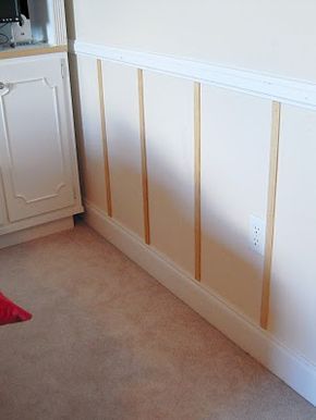 a room with white walls and wooden paneling on the wall, next to a red pillow