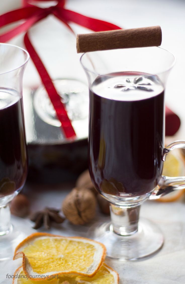 two glasses filled with mulled and cinnamon sitting on a table next to an orange slice