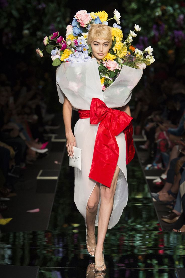 a woman with flowers on her head walking down the runway at moschino fashion show