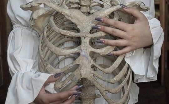 a woman holding a human skeleton in her hands with both hands on the ribcage