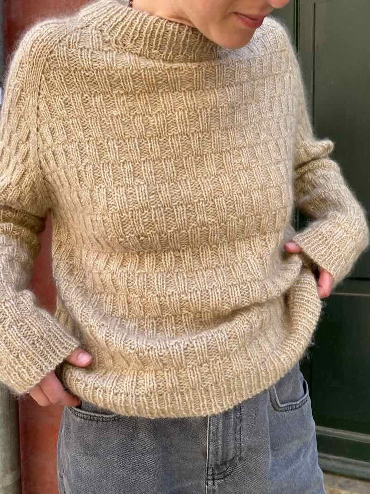 a woman standing in front of a door with her hands on her hips wearing a sweater