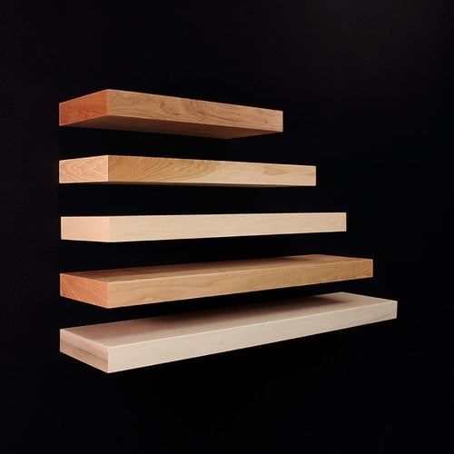 three wooden shelves stacked on top of each other in front of a black wall with light coming through