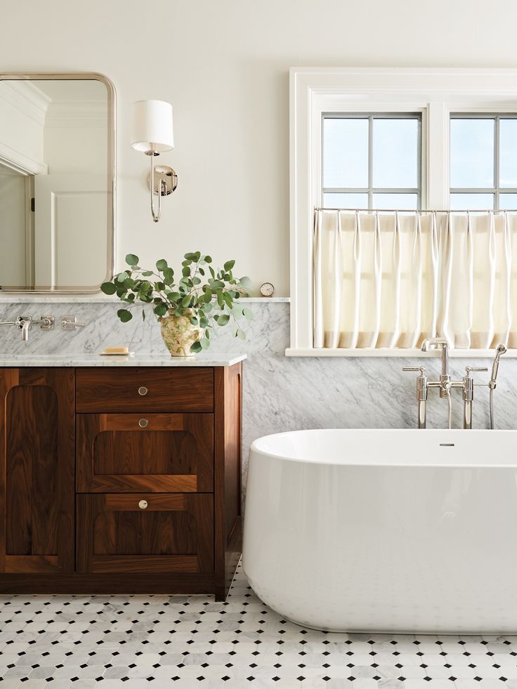 a white bath tub sitting next to a bathroom sink under a window with two windows