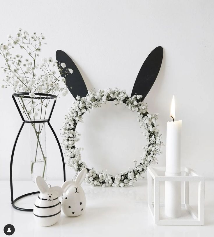 a white table topped with a vase filled with flowers next to a bunny head wreath