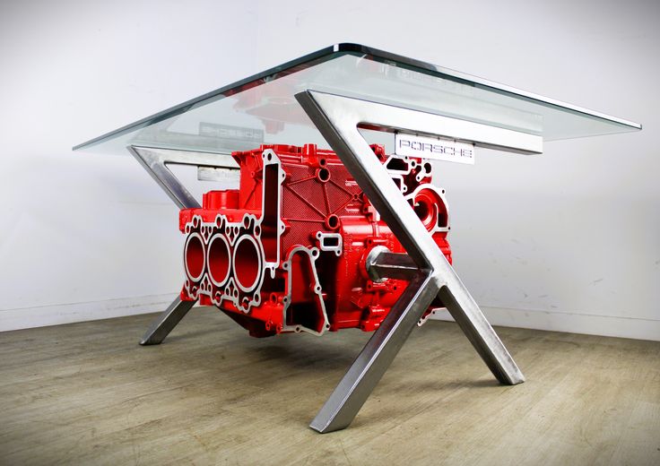 a red engine sitting on top of a wooden floor next to a glass table with metal legs