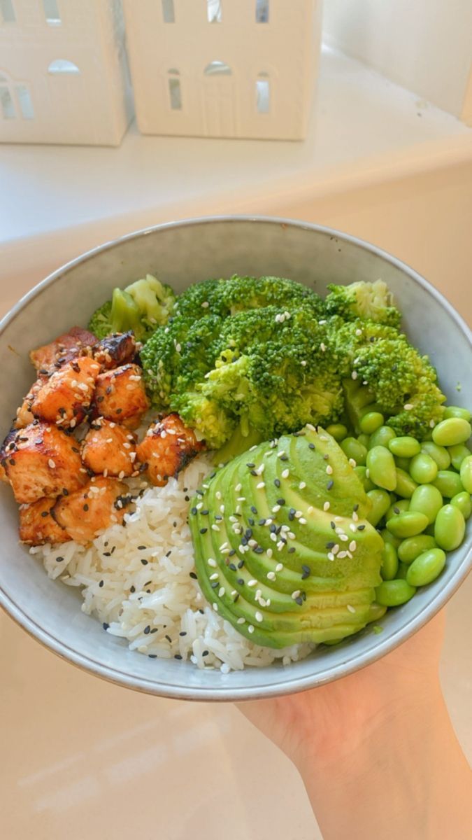 someone holding up a bowl with rice, broccoli and chicken