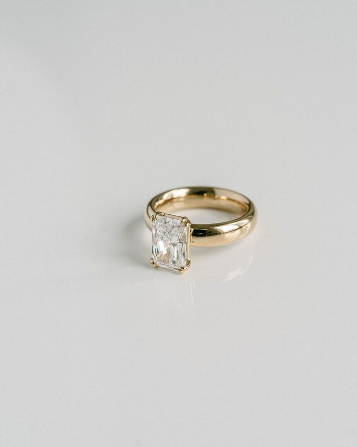 a yellow gold engagement ring with a princess cut diamond in the center, on a white background