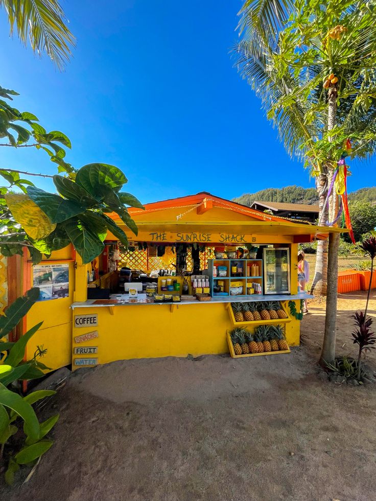 a small yellow stand on the side of a dirt road with trees in front of it