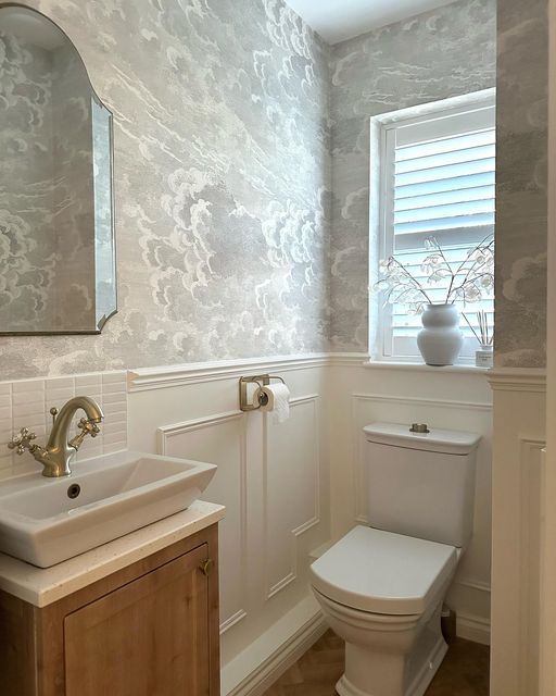 a white toilet sitting next to a sink in a bathroom under a mirror and a window