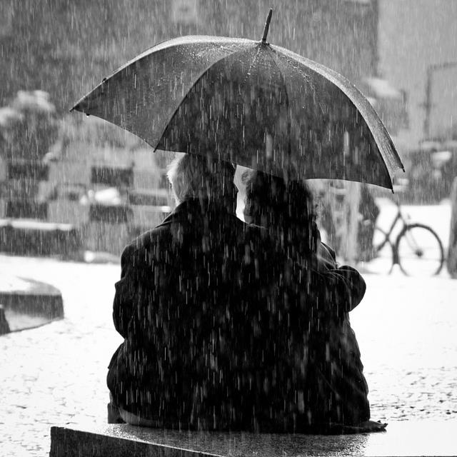 two people sitting on a bench under an umbrella in the rain with words written below