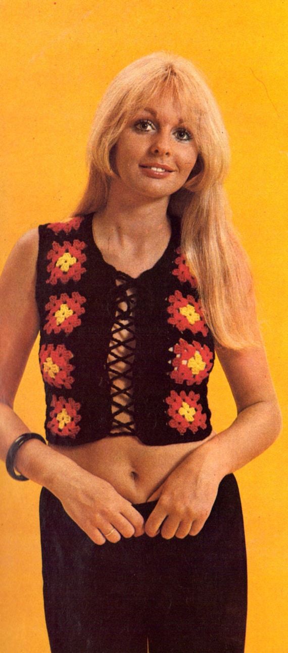 a woman with long blonde hair wearing a crocheted crop top and black pants