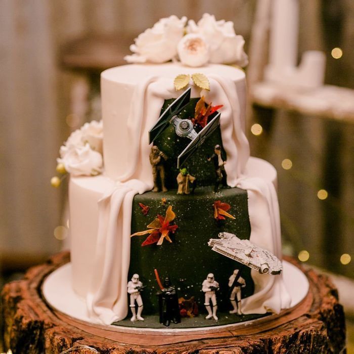 a star wars themed wedding cake on top of a tree stump with lights in the background