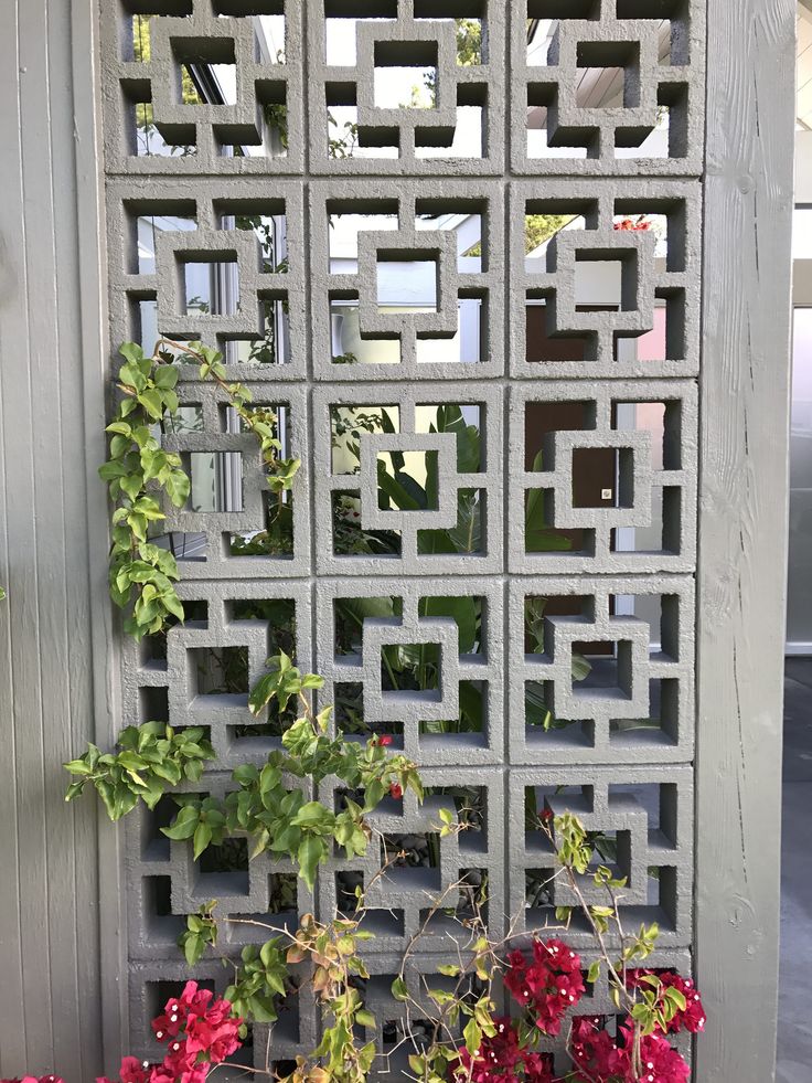 some red flowers and green plants in front of a gray wall with an intricate lattice design