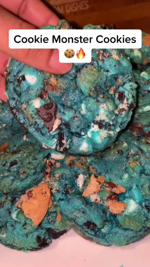 someone is holding up some cookies with blue icing and chocolate chips on them, in front of a white plate